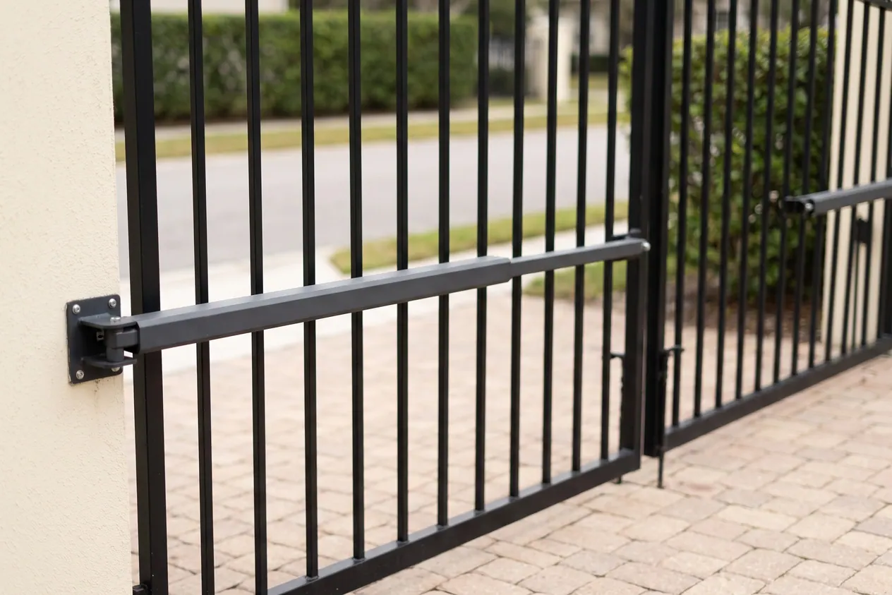 An operator arm fixed to the house side of a black iron swing gate leaf